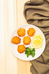 Homemade red fish cakes with lemon and parsley in ceramic plate. With fabric drapery on wooden background, top view.