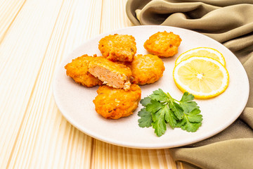Homemade red fish cakes with lemon and parsley in ceramic plate. With fabric drapery on wooden background, close up.