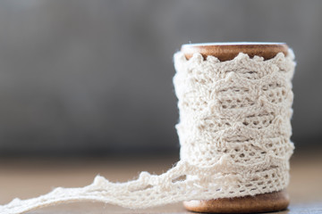 close up wooden spool with white lace, ribbon, on wooden table, grey background. Copy space