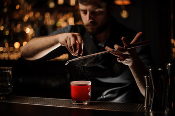 Fototapeta na wymiar Bartender adding to a red cocktail in the glass a grated nutmeg