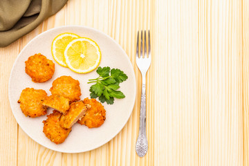 Homemade red fish cakes with lemon and parsley in ceramic plate. With fabric drapery and fork on wooden background, top view, copy space.