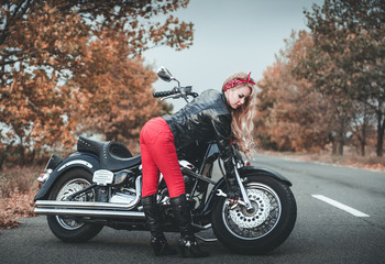 Young beautiful caucasian woman posing with motorcycle on the road.