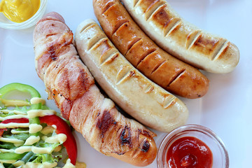 Top view of German Pork Sausages and salad vegetables with sauce in the white plate background. Foods concept.
