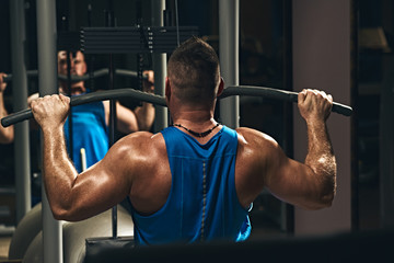 Strong male bodybuilder doing exercise for back with lat pulldown machine in gym