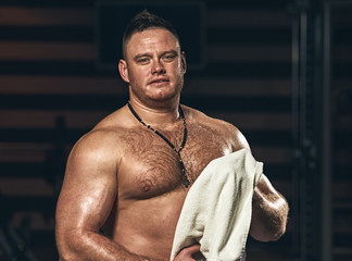 Tired athletic muscular man with towel resting in gym