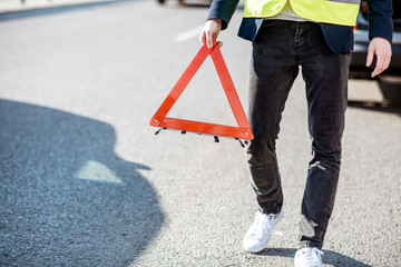 Man carrying emergency triangle sign on the road, having a problem with his car, close-up view