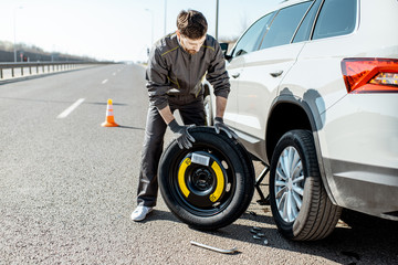 Road assistance worker in uniform changing car wheel on the highway