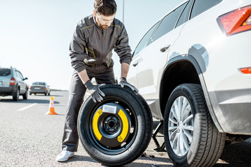 Road assistance worker in uniform changing car wheel on the highway