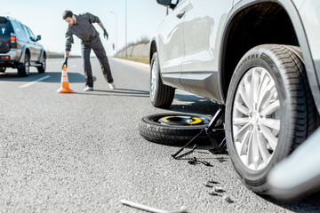 Road assistance worker putting emergency cones near the broken car on the highway