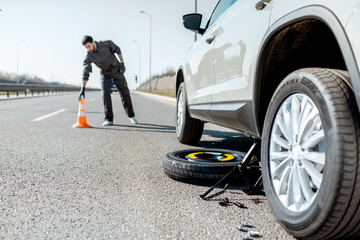 Road assistance worker putting emergency cones near the broken car on the highway