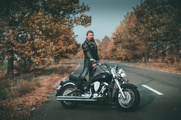 Stylish biker posing with motorcycle on the road.