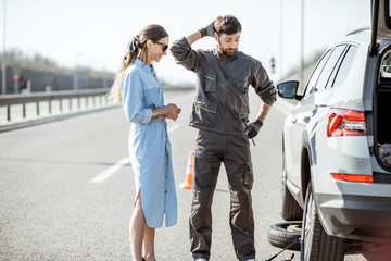 Fototapeta na wymiar Road assistance worker in uniform with young woman standing near the broken car on the highway