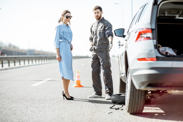 Road assistance worker in uniform with young woman standing near the broken car on the highway
