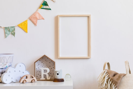 The modern scandinavian newborn baby room with mock up photo frame, wooden toy, design accessories and natural basket. Hanging cotton colorful flags. Minimalistic and cozy interior of child room. 