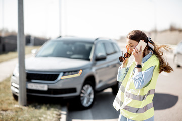 Embarrassed woman calling road assistance standing near the car during the road accident on the highway