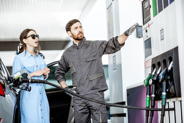 Young woman client with gas station worker refueling car at the gas station