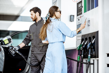 Woman paying with phone for gasoline, photographing bar code at the gas station with worker on the background