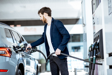 Businessman refueling his luxury car holding filling gun at the gas station