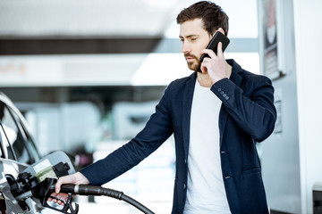 Businessman talking with phone while refueling car at the gas station