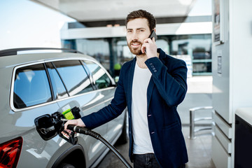 Businessman talking with phone while refueling car at the gas station
