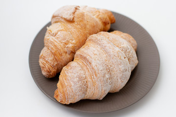 breakfast croissants sprinkled with powdered sugar on a gray plate. white background