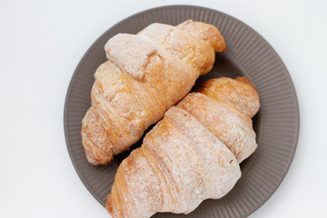 breakfast croissants sprinkled with powdered sugar on a gray plate. white background