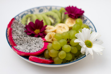 tropical assorted fruits on a blue plate. White background. dragonfruit, banana, green grape and kiwi 