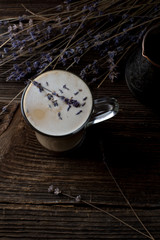 Low key photo of lavender latte or raf coffee in transparent cup with lavender twigs on background, close up, back light. Trendy dark and moody style