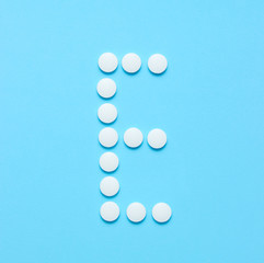 Vitamin E. Letter E from white pills on blue background. Minimalistic medical concept. Top view.