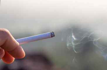 Hand of man with burning smoldering cigarette.