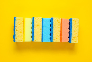 Horizontal stack of colored cleaning sponges isolated on yellow background. Minimalistic cleaning concept