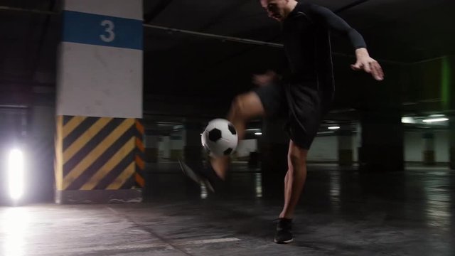 Underground parking lot. A young soccer man training his football skills