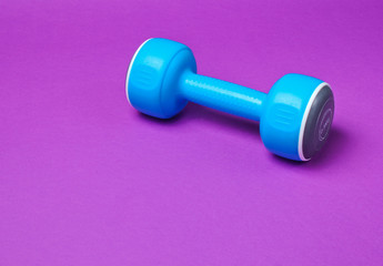 Obraz premium One blue plastic dumbbell on a purple background.