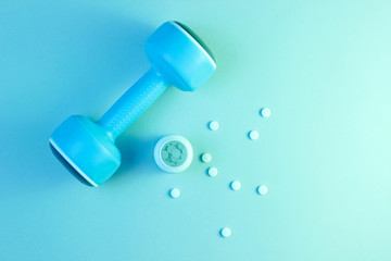Minimalism sports pharmacology concept. Blue plastic dumbbell and bottle with white vitamin pills,...