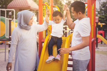 Parents guide their daughter to play with a slide