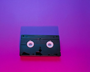 Retro wave style video cassette with neon pink-violet light. 80s. Top view