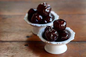 Sweet Jujube or Chinese red date in syrup in white Thai style cup on wood table and space for write wording, Clever idea for fresh fruit preservation, popular sweet, unhealthy food cause of disease