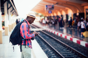 African man traveler standing and using smartphone waiting for the train on railroad station