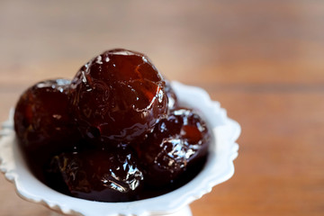 Sweet Jujube or Chinese red date in syrup in white Thai style cup on wood table and space for write wording, Clever idea for fresh fruit preservation, popular sweet, unhealthy food cause of disease