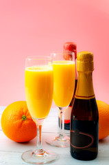 Lush mix drinks, summer alcoholic beverages and refreshing brunch cocktail concept theme with champagne flutes, orange fruits and bottles of bubbly isolated on white wooden table and pink background