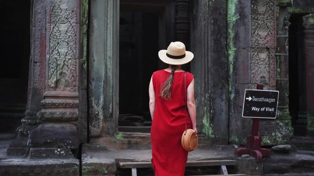 Attractive young woman entering the temple in the red dress. Shot from the back of a woman in the red dress walking into the temple in Cambodia, Angkor, Ta Prohm Temple. 