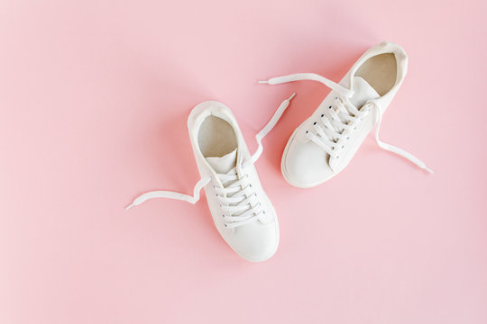 White female sneakers on pink background. Flat lay, top view minimal background. Fashion blog or magazine concept.