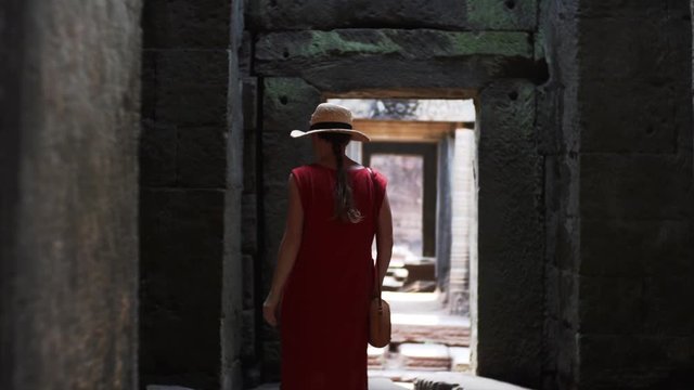 Attractive young woman walking through the temple morning. Woman in the red dress admiring the temple in Cambodia, Angkor, Ta Prohm Temple. 