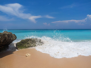 Fototapeta na wymiar Turquoise waves crash against stones with splashes. Bali.