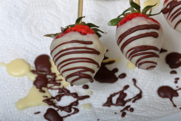 Strawberries glazed in black and white chocolate dries on a plate. On the work surface visible drops of chocolate. Cooking strawberries glazed in chocolate.