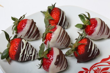 Strawberries glazed in black and white chocolate. Lie on a white plate with a pattern.