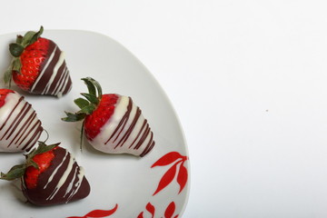 Strawberries glazed in black and white chocolate. Lie on a white plate with a pattern.