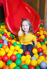 Fototapeta na wymiar Happy little girl playing and having fun at kindergarten with colorful balls and show thumb up in play center
