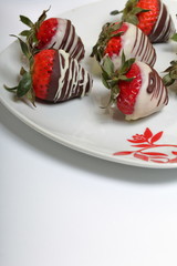 Strawberries glazed in black and white chocolate. Lie on a white plate with a pattern.