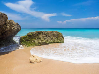 Turquoise waves crash against stones with splashes. Bali.